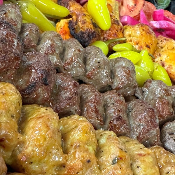 Close-up of grilled Mediterranean kabobs, including chicken and beef, with pickled peppers and vegetables.