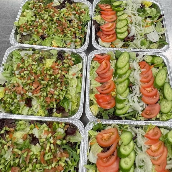 Six foil trays of fresh Mediterranean salads with lettuce, diced cucumbers, tomatoes, and onions.