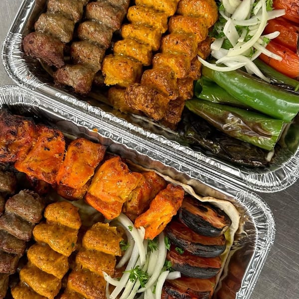 Two foil trays filled with various grilled kabobs, vegetables, and onions from York Kabob.
